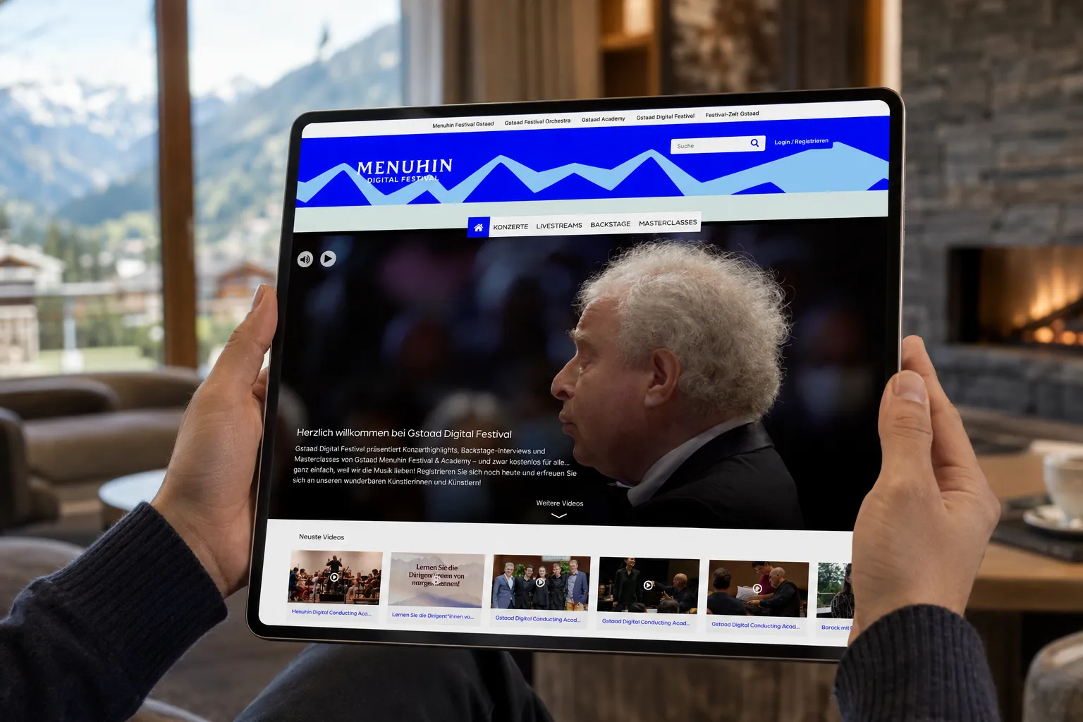 Gstaad Digital Festival auf einem Tablet, im Hintergrund ein Fenster mit Blick auf die Berge um Gstaad